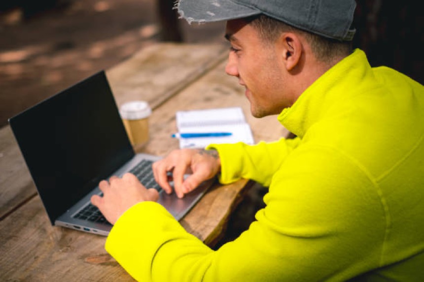 Persoon in felgele trui werkt buiten op een laptop.